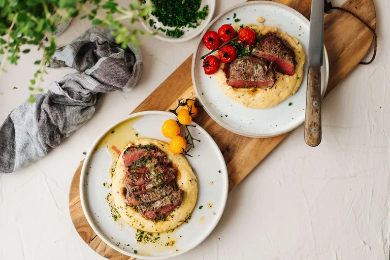 Rosa gebratenes Rindersteak auf cremiger Polenta mit geschmorten Tomaten