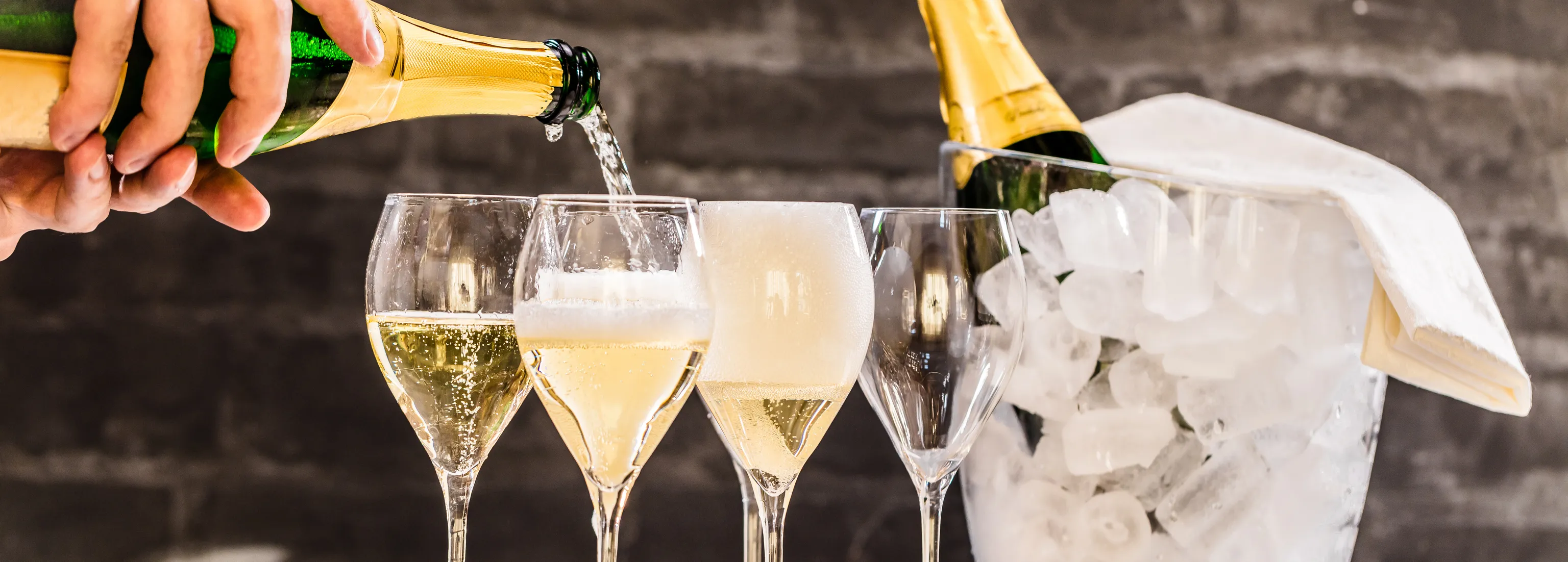 Es sind mehrere Sektgläser zu sehen und in ein Glas wird gerade Sekt eingeschenkt.