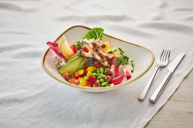 Ein farbenfroher Salat mit Avocado, Pilzen, Radieschen, Gurke, Rotkohl und Nüssen in einer Schüssel auf einem Tisch, dazu eine Gabel und ein Messer.