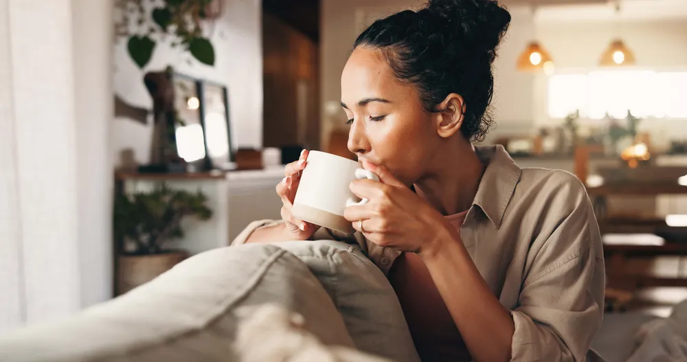 Frau sitzt entspannt auf dem Sofa und genießt eine Tasse heißen Tee in gemütlicher Wohnatmosphäre
