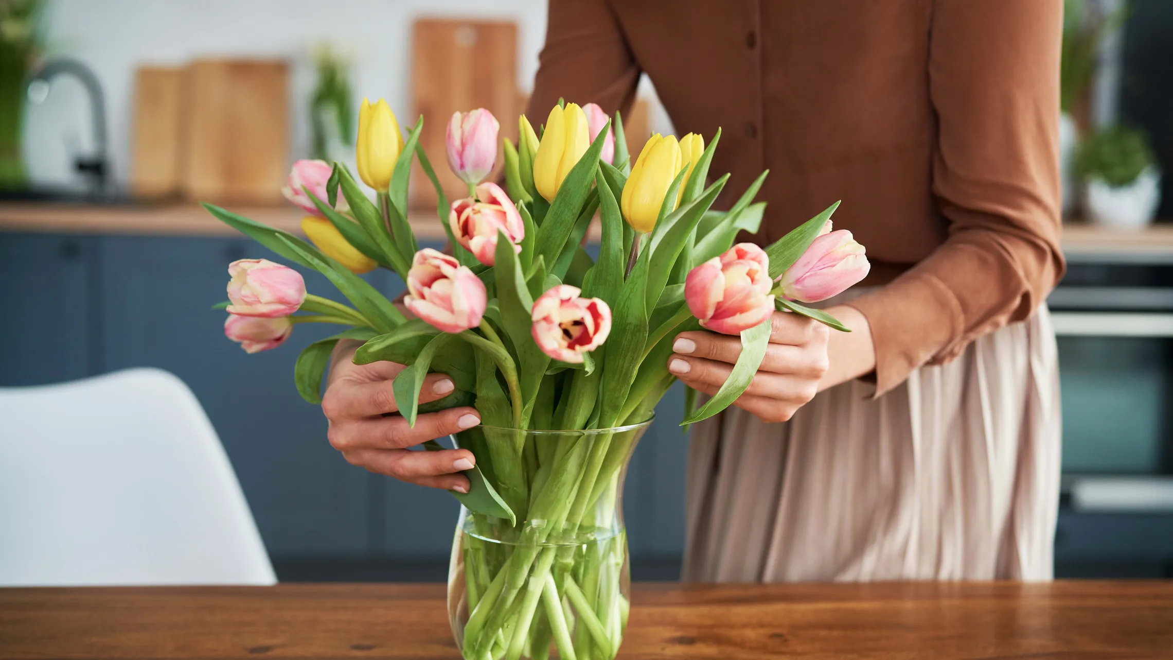 Eine Frau arrangiert einen Tulpenstrauß an einem braunen Holztisch