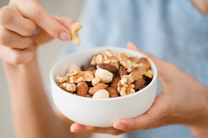 Hand hält eine Schüssel mit gemischten Nüssen aus Mandeln, Walnüssen und Cashews als gesunden Snack.