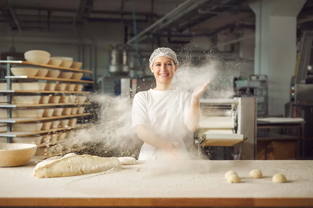 Bäckerin in einer Backstube bei der Arbeit mit Teig und Mehl