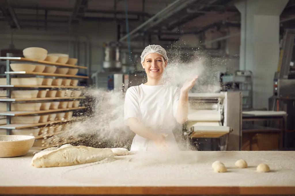 Bäckerin in einer Backstube bei der Arbeit mit Teig und Mehl