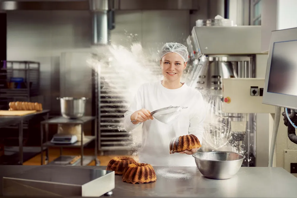 Konditorin bestäubt frisch gebackenen Kuchen in der Backstube mit Staubzucker