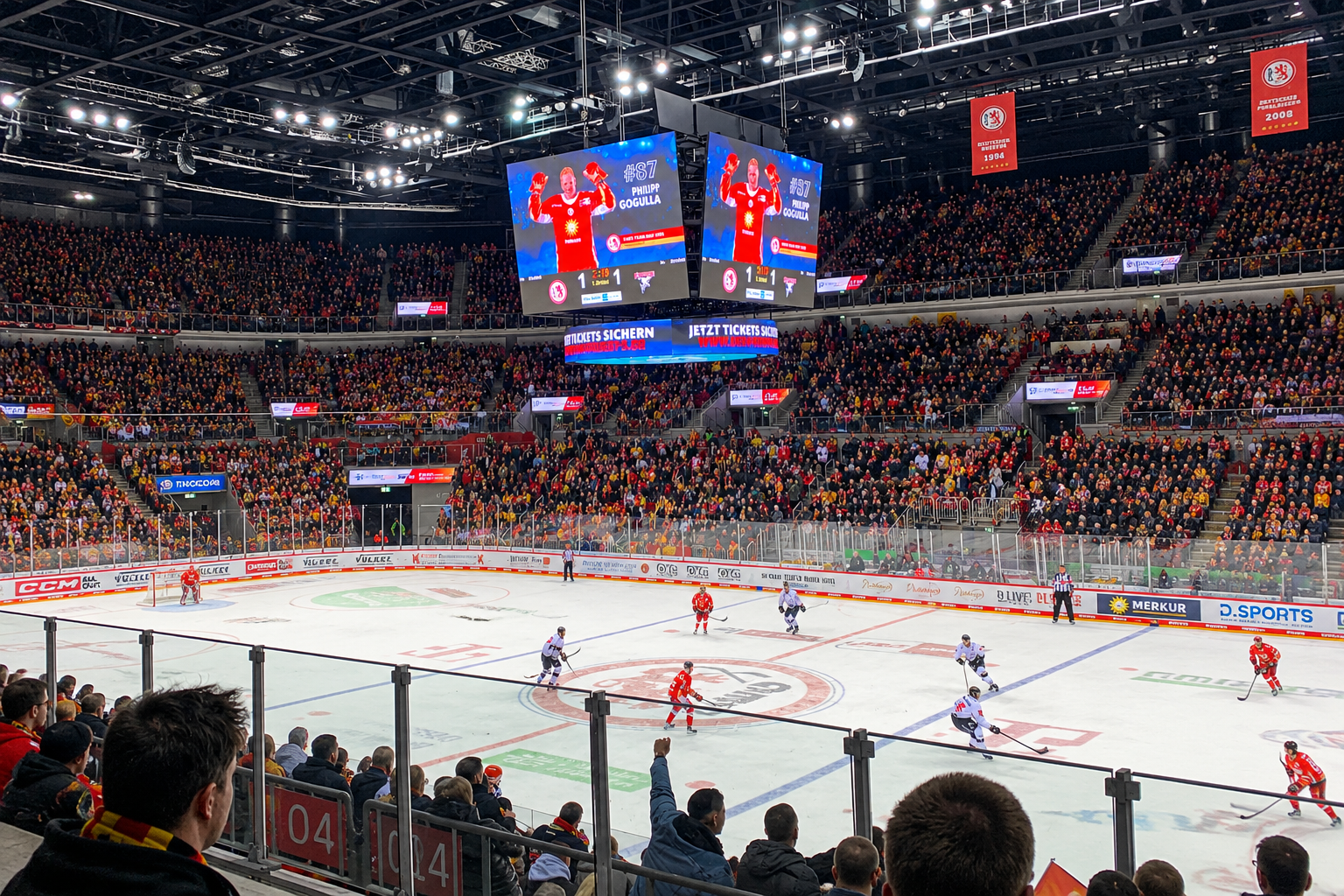 Ein vollbesetztes Stadion bei einem Eishockeyspiel, ein großes Display zeigt Informationen über einen Spieler, während Teams auf dem Eis spielen.