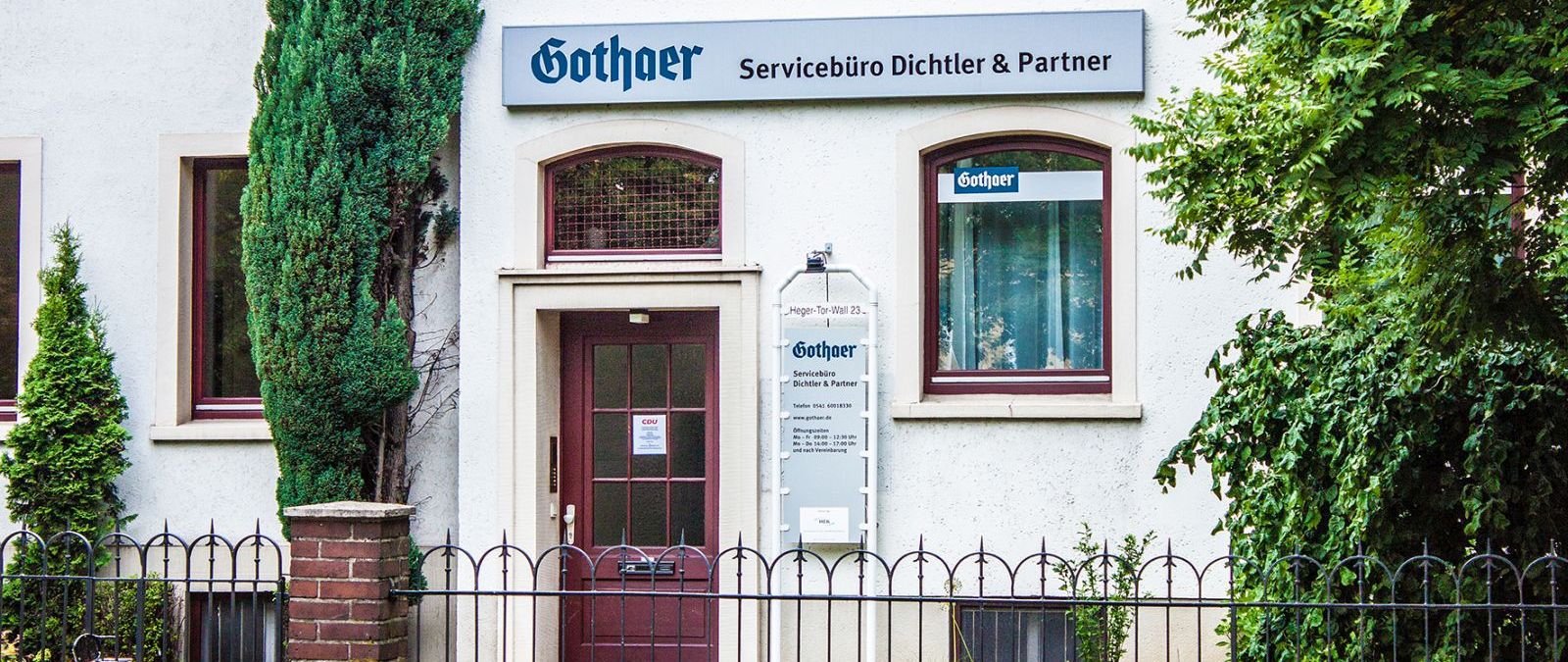 Eingang eines Servicebüros mit Schildern der Firma Gothaer und CDU, umgeben von Pflanzen und einem niedrigen Zaun. - Daniel Dichtler, BarmeniaGothaer Osnabrück