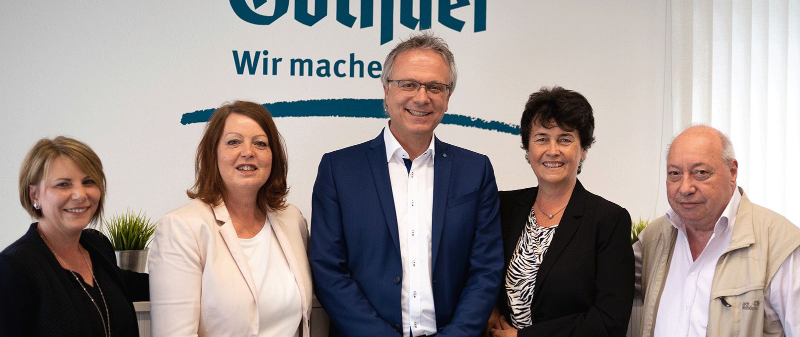 Fünf Personen stehen Seite an Seite vor einem Firmenlogo an einer Wand, alle lächeln in die Kamera. - Martin Süs, BarmeniaGothaer St. Wendel