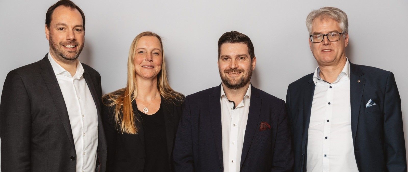Vier Personen in Businesskleidung stehen nebeneinander vor einem neutralen Hintergrund und lächeln in die Kamera. - Christian Laturnus, BarmeniaGothaer Oldenburg