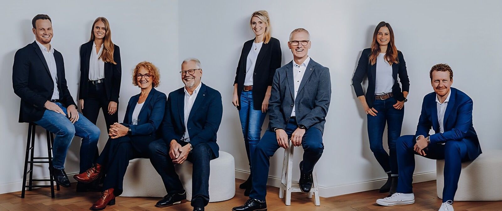 Acht Personen in formeller Kleidung posieren in einem Raum, einige sitzen, andere stehen, alle lächeln. - Thorben Walterskötter, BarmeniaGothaer Ibbenbüren