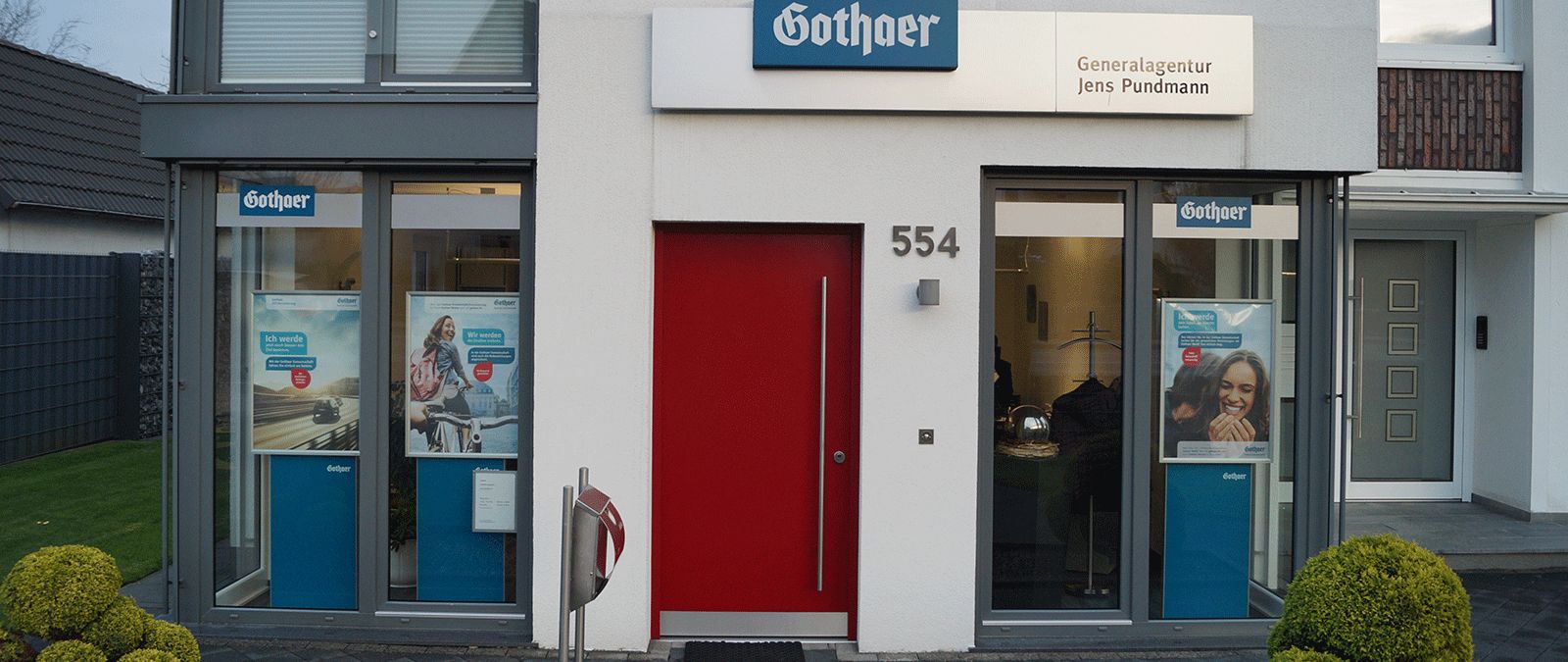 Außenansicht einer Gothaer Versicherungsagentur mit großen Fenstern, Poster im Schaufenster und einer roten Eingangstür. - Jens Pundmann, BarmeniaGothaer Bielefeld