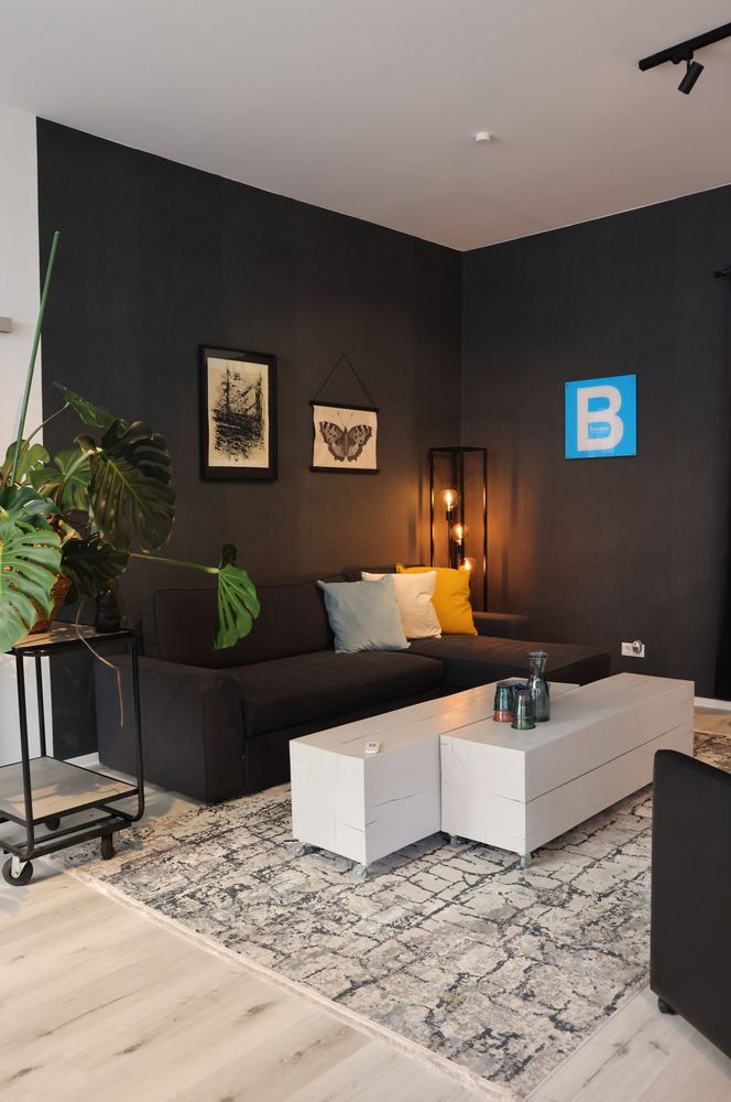 Modernes Wohnzimmer mit dunkler Wandfarbe, grauem Sofa, weißen Tischen, dekorativer Beleuchtung und Pflanzen. Bilder an der Wand. - Naja Piechaczek, BarmeniaGothaer Wuppertal