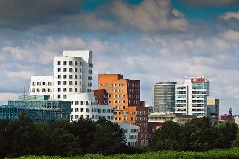 Moderne Gebäude mit weißer und roter Fassade, umgeben von grünen Bäumen und unter einem bewölkten Himmel.