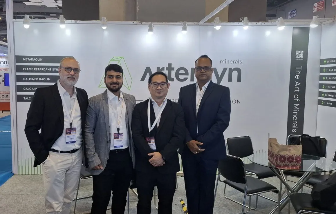 Four men in business attire pose in front of an "Arteryn minerals" booth at a trade show