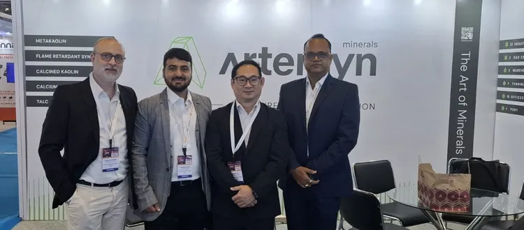Four men in business attire pose in front of an "Arteryn minerals" booth at a trade show