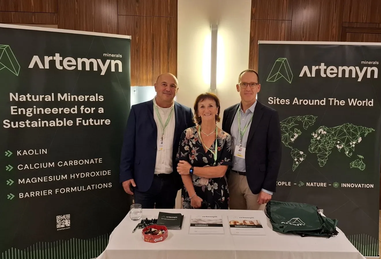 Three people stand at an Artemyn minerals booth with banners highlighting natural minerals for sustainability, products, and global sites.