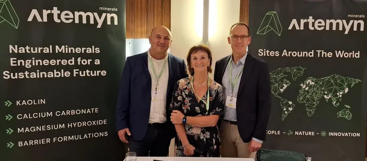 Three people stand at an Artemyn minerals booth with banners highlighting natural minerals for sustainability, products, and global sites.
