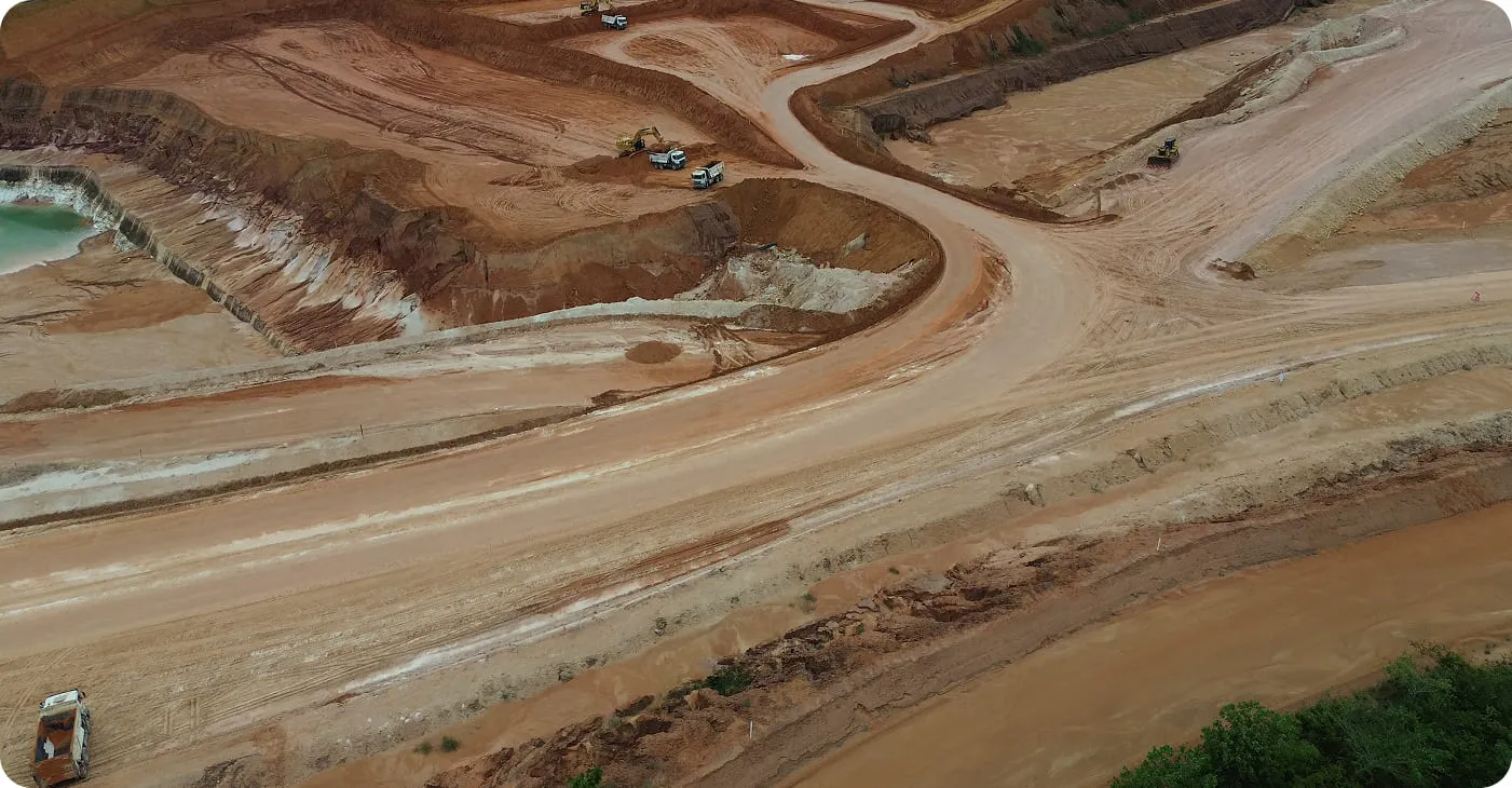 Aerial view of a large construction site with exposed earth, heavy machinery, and dirt roads winding through the site.