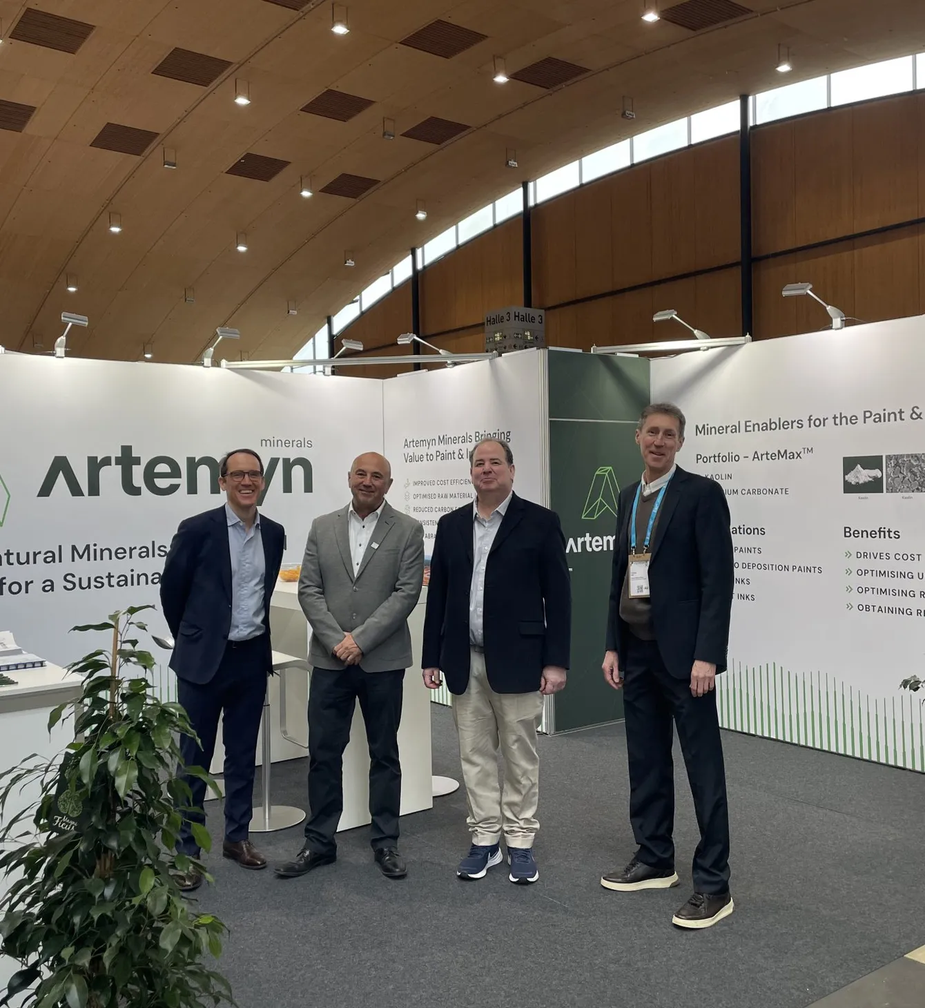 Four men stand in front of an Artemyn Minerals exhibition booth, displaying information on mineral enablers for the paint and ink market.