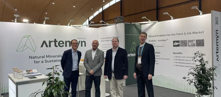 Four men stand in front of an Artemyn Minerals exhibition booth, displaying information on mineral enablers for the paint and ink market.