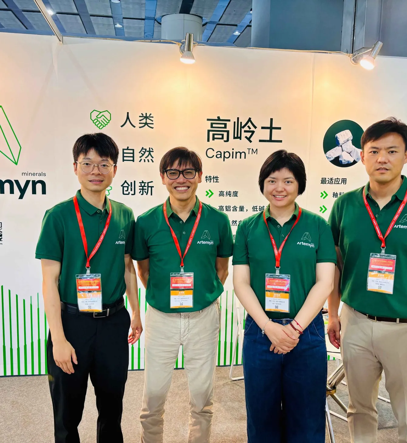 Four people in green Artemyn shirts with red lanyards pose at a trade booth featuring the company's logo and product information.