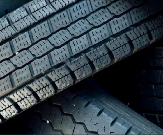 Close-up of stacked black tires, showcasing detailed tread patterns and textures, arranged at angles.