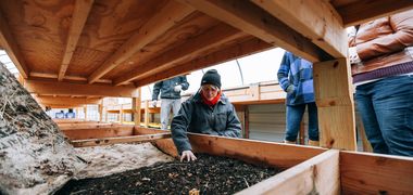 Eine Frau prüft die Zusammensetzung von Erde in einem Holzkasten.