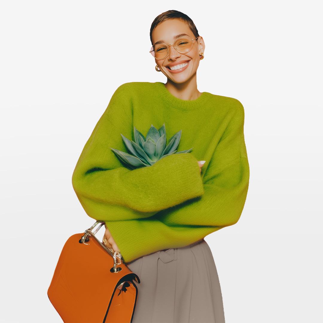 Person in a bright green sweater holding a succulent plant, smiling, with an orange handbag on their arm.