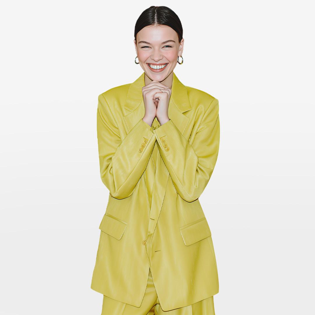 Smiling person in a bright yellow suit with clasped hands, standing against a plain white background.