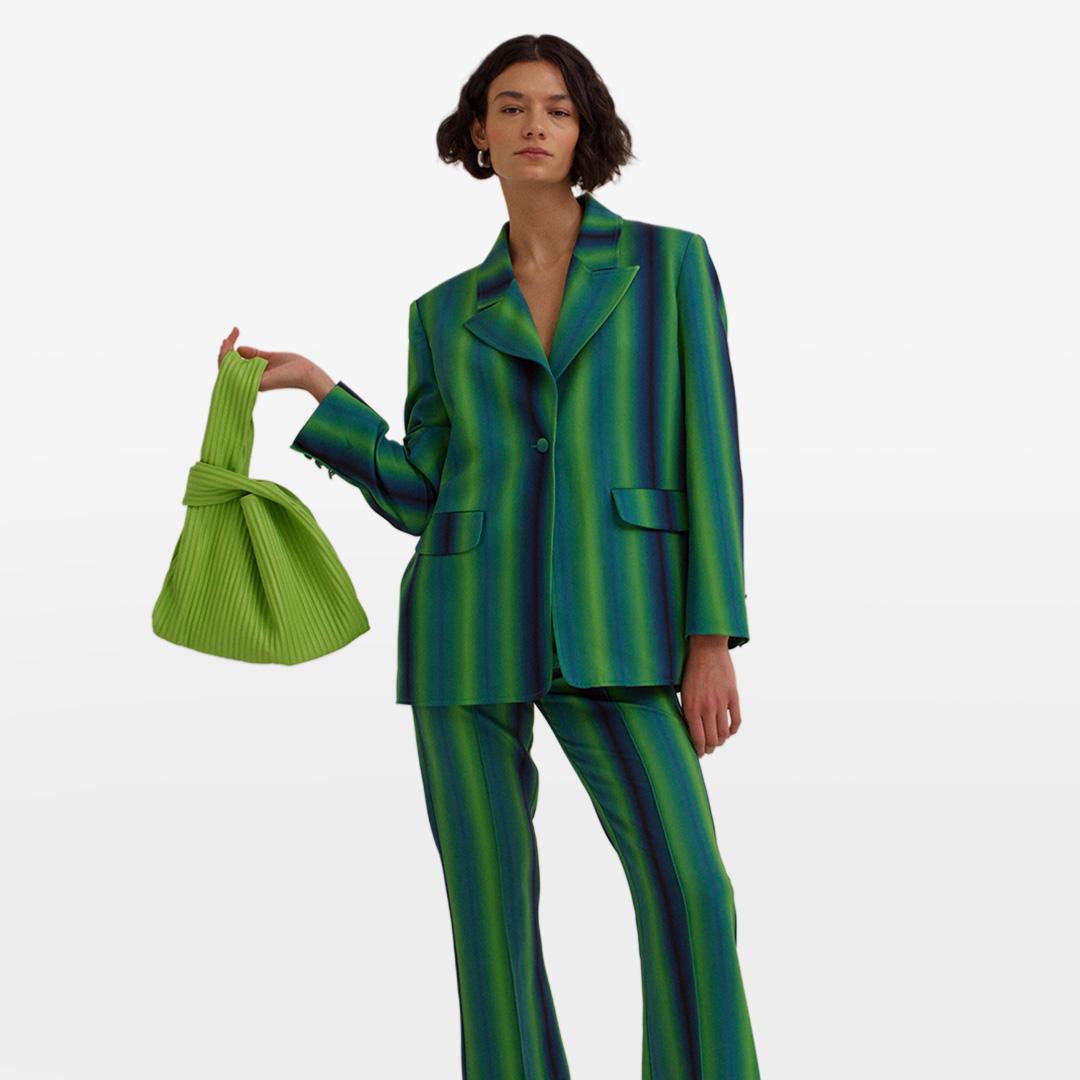 A person in a green and blue striped suit holds a matching green pleated handbag against a plain background.