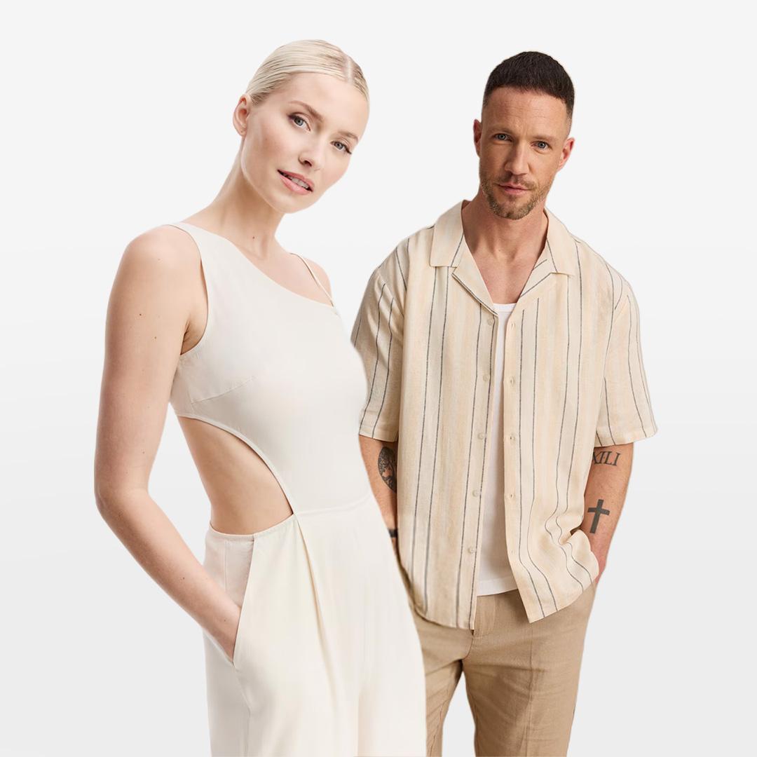A woman in a white sleeveless dress with side cutouts and a man in a beige striped shirt and tan pants stand against a white background.