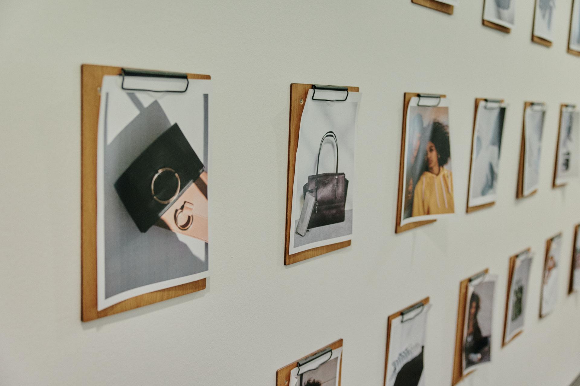 Photos displayed on a wall in wooden clip frames, showcasing fashion items and portraits.