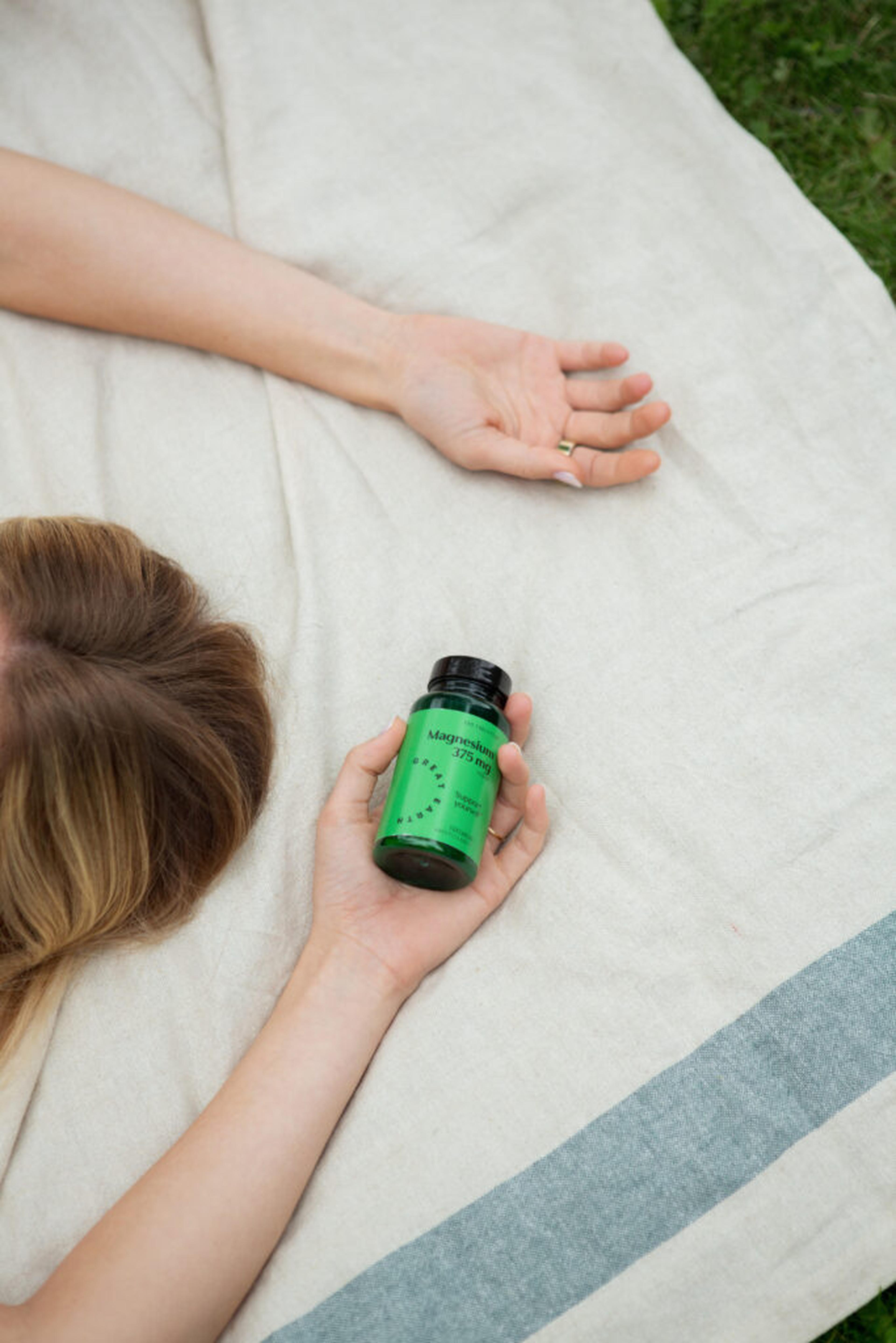Kvinna som ligger på en filt i gräset och håller en burk Great Earth Magnesium