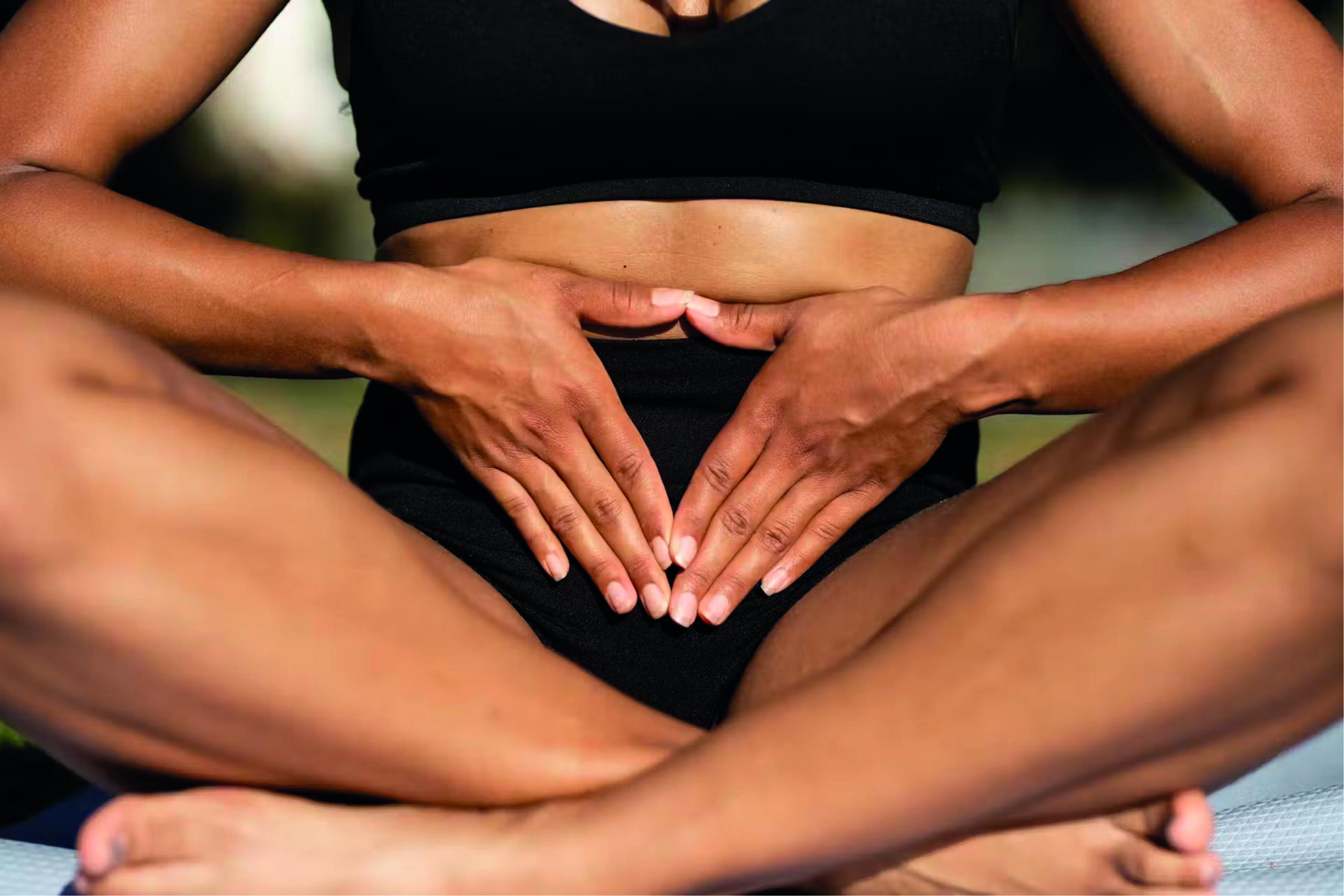 Woman sitting cross-legged with her hands placed gently over her lower abdomen