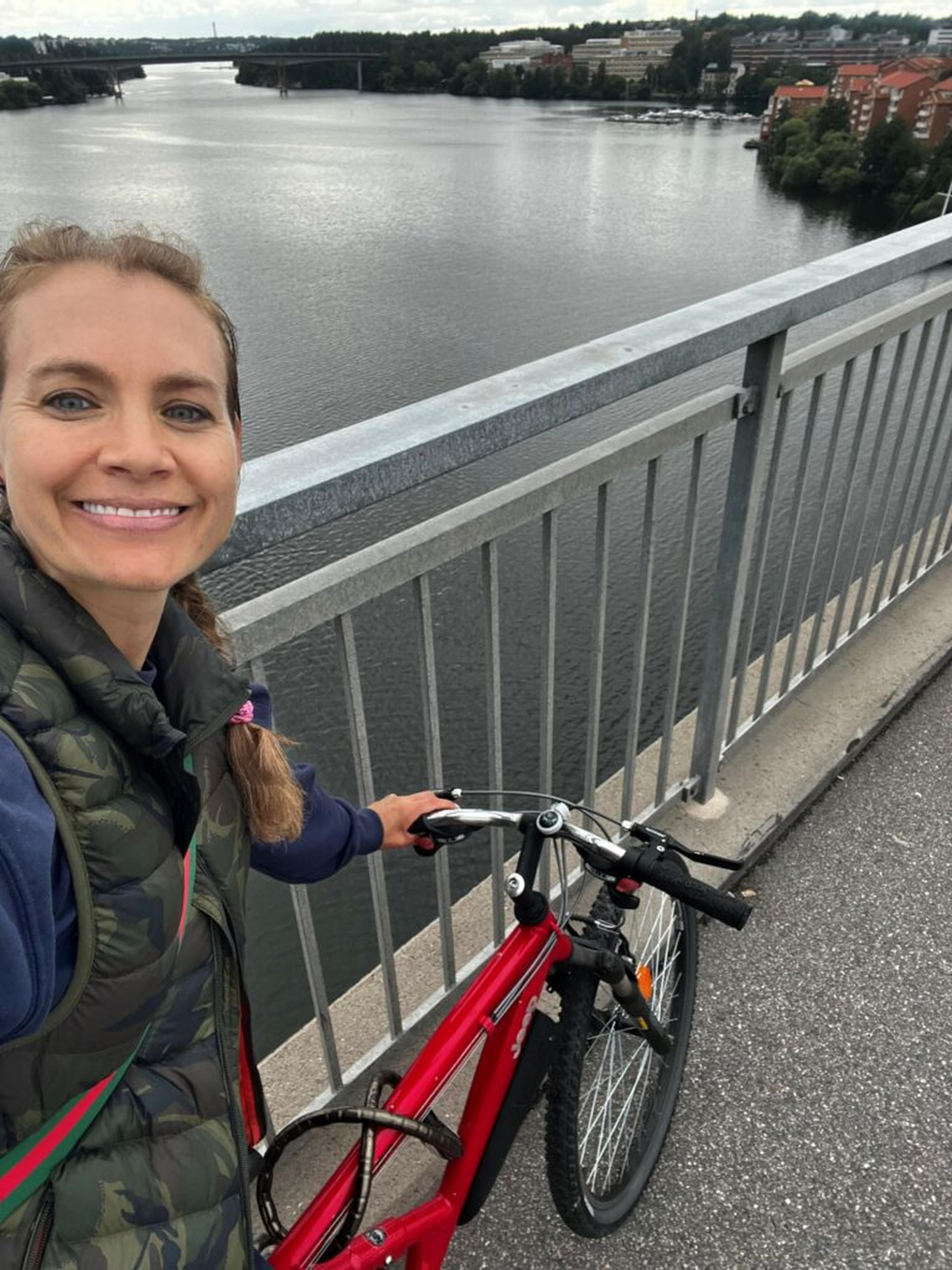 Leende kvinna som står med en röd cykel på en bro över vatten