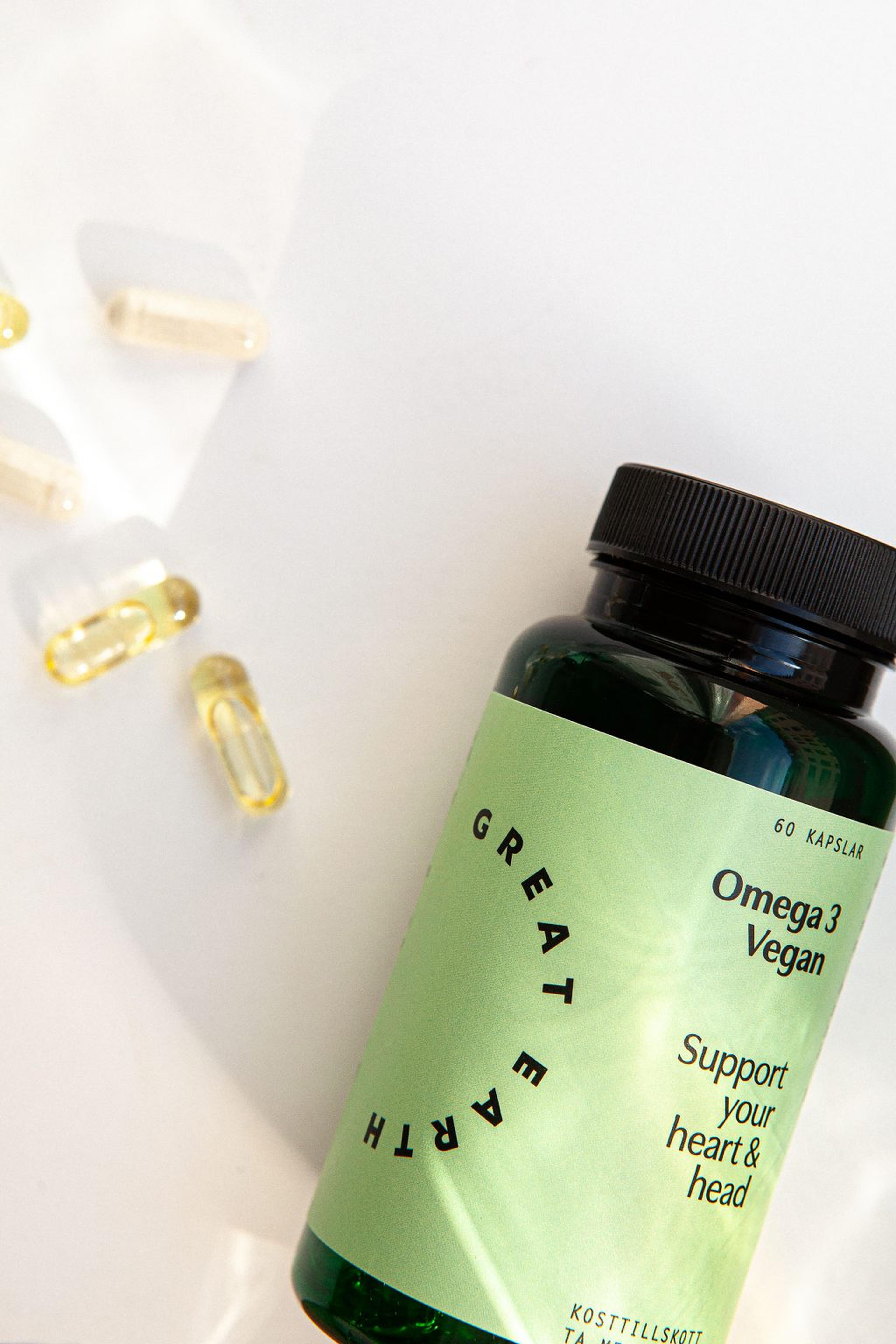 En burk Great Earth Omega 3 Vegan som ligger på en ljus yta med utspridda gula mjukkapslar