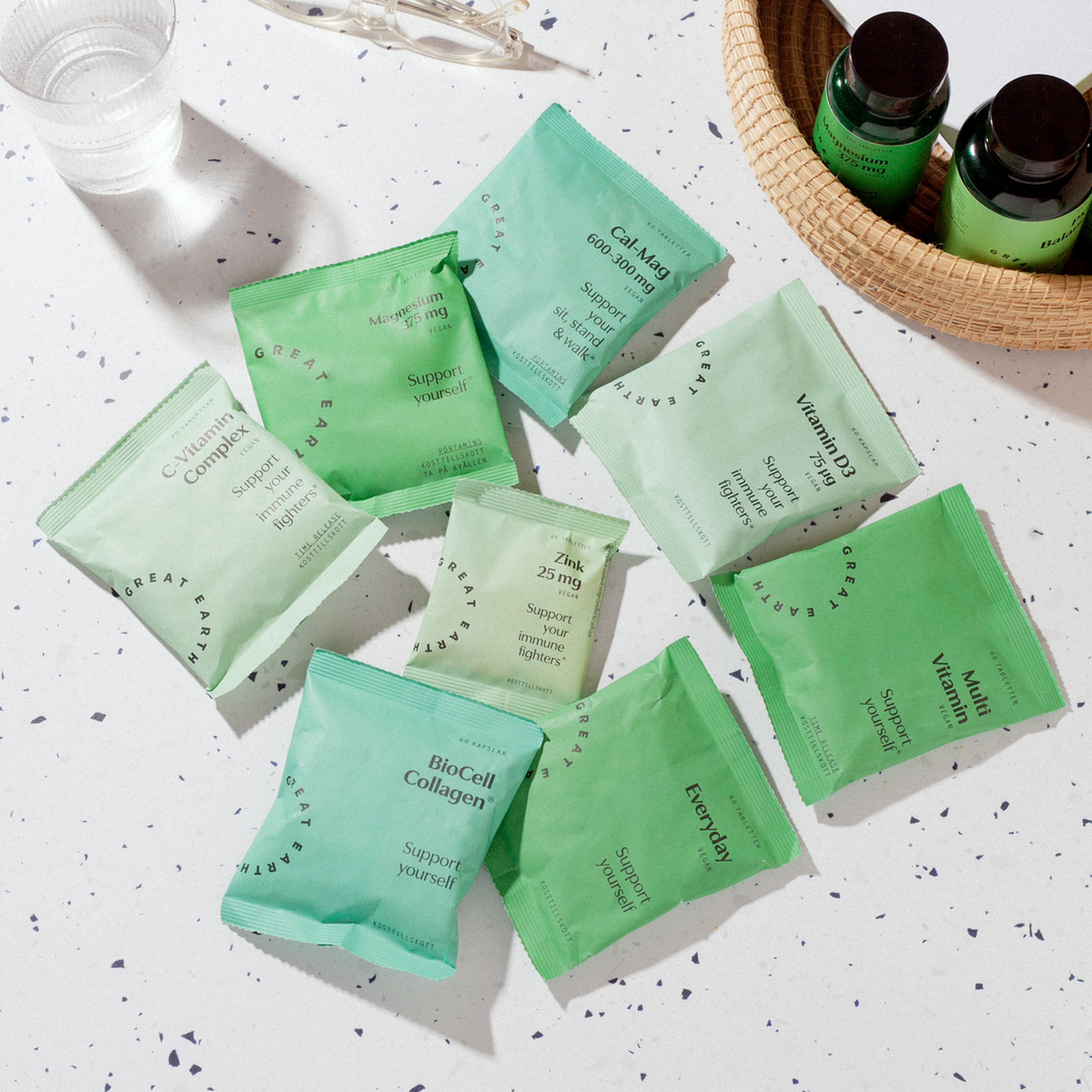Green supplement pouches and bottles from Great Earth on a speckled table next to a glass of water