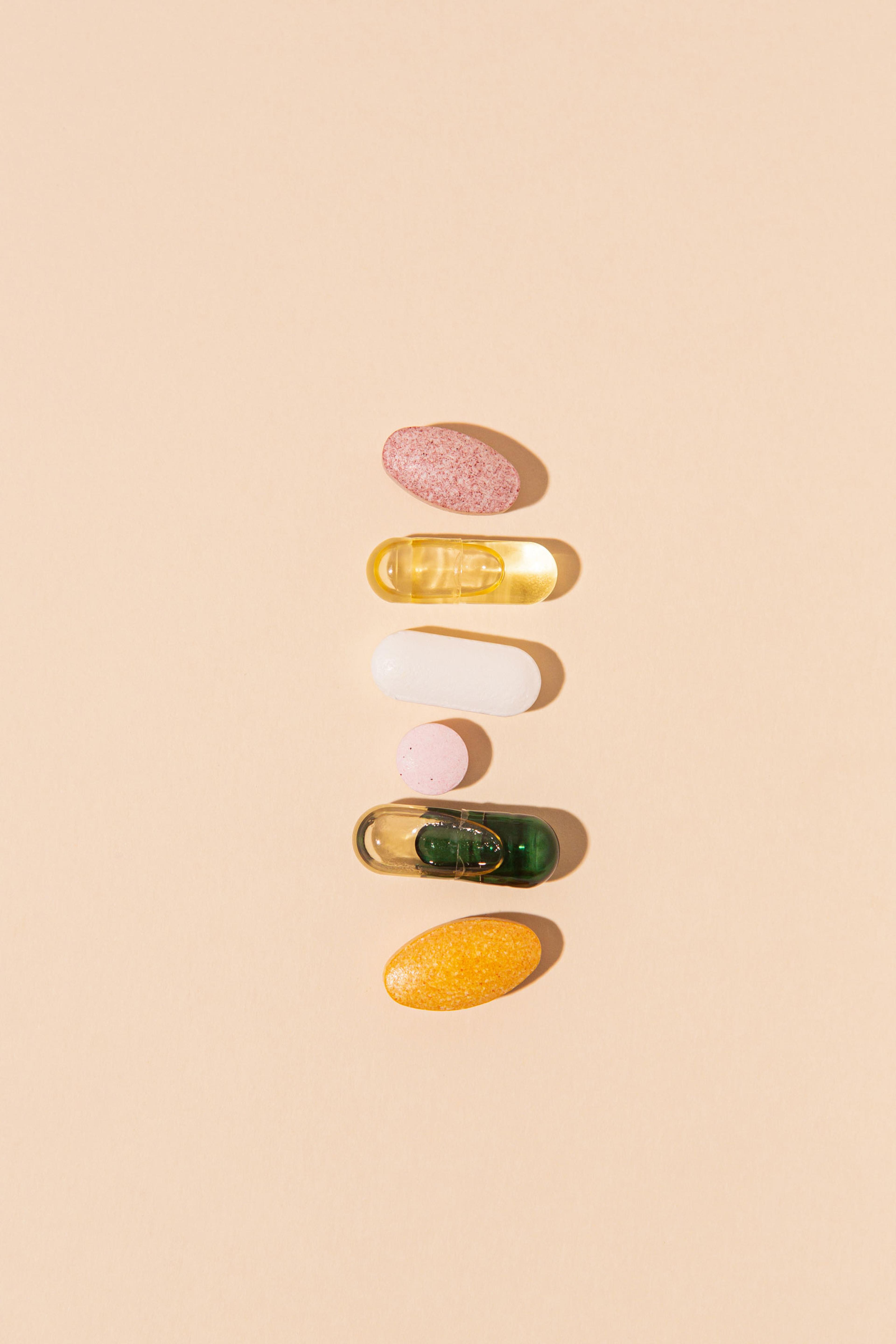 Six different supplement tablets and capsules arranged in a vertical row on a beige background