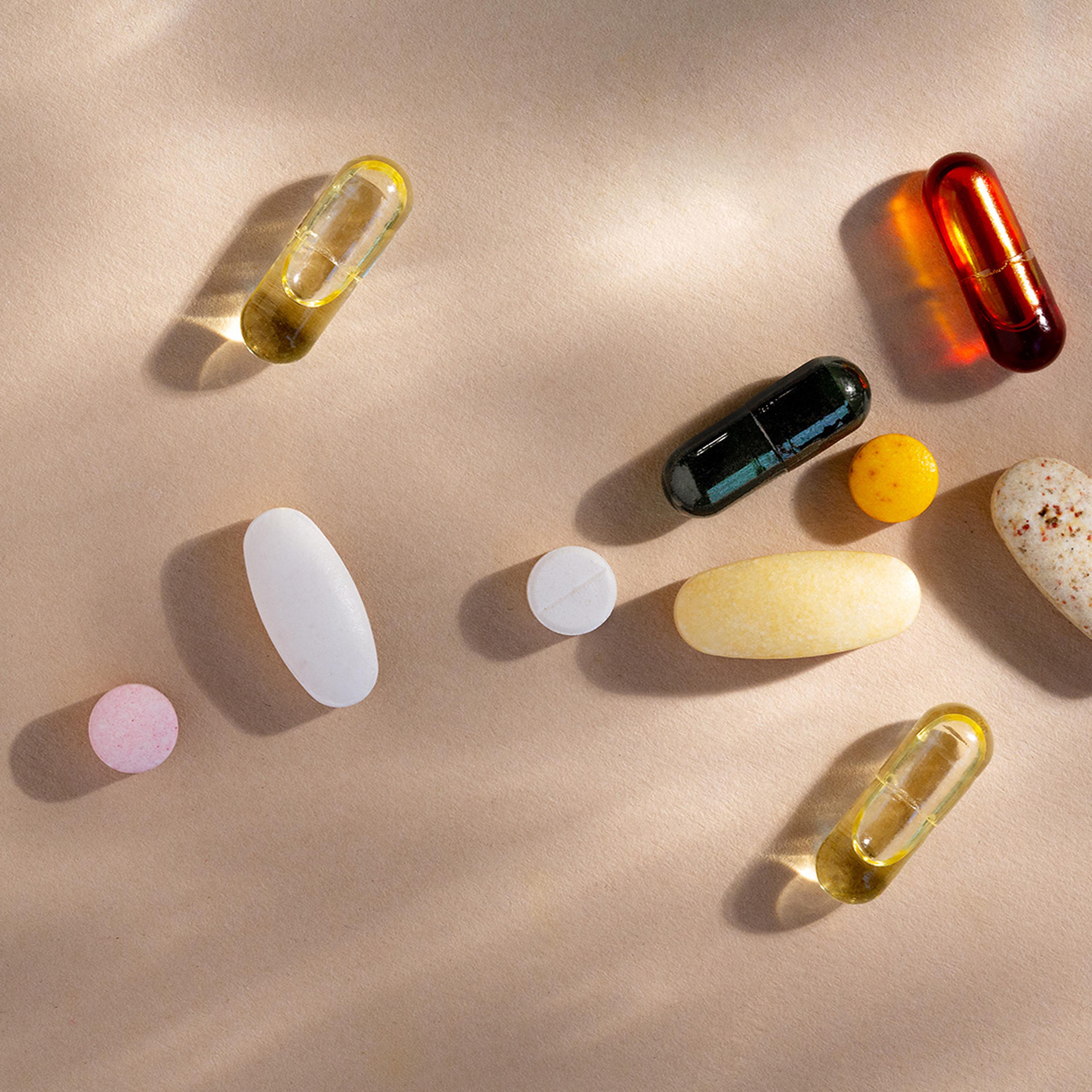 Färgglada vitamintabletter och kapslar i olika former utspridda på en beige yta