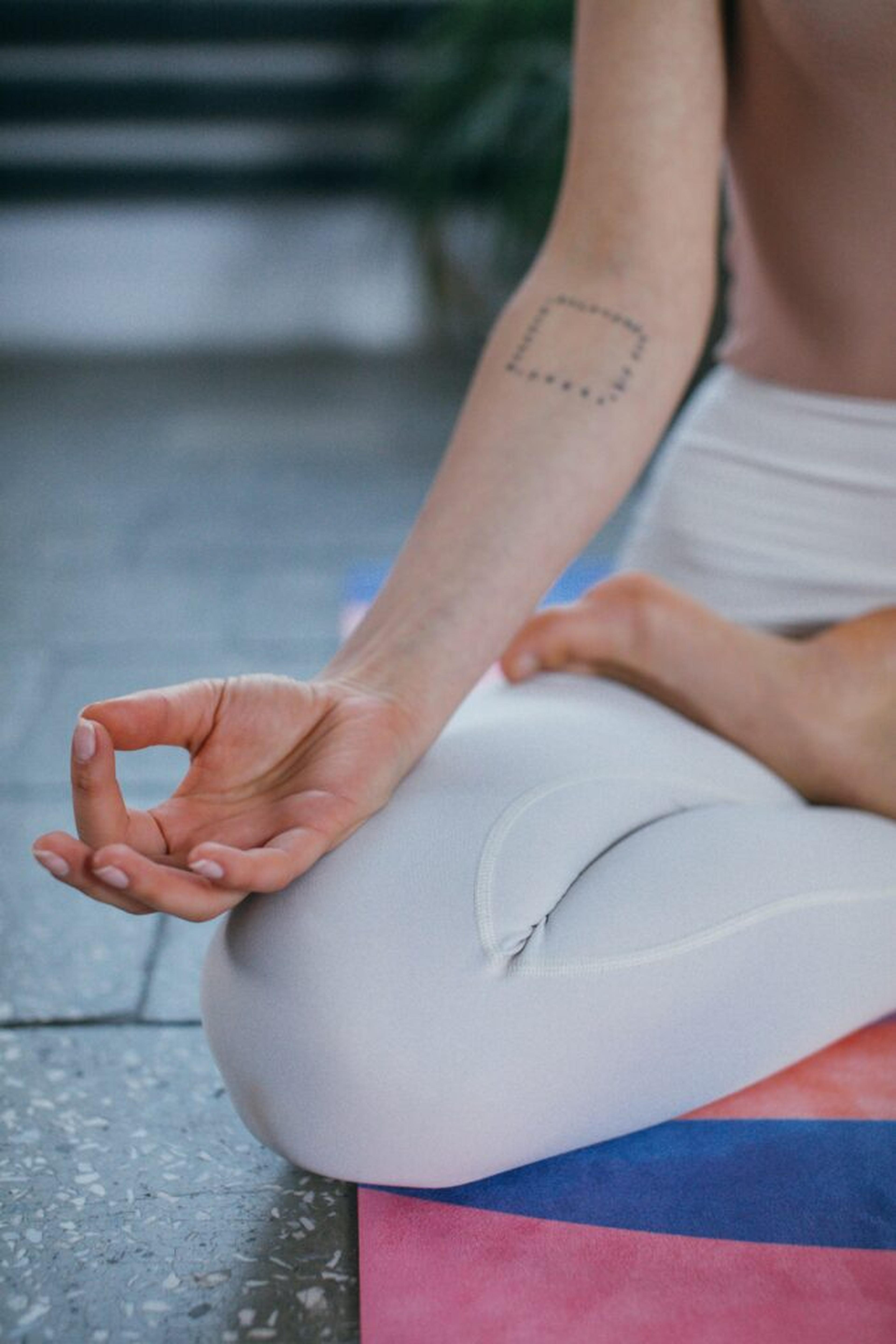 Person som sitter i meditationsposition på en yogamatta med handen i mudra