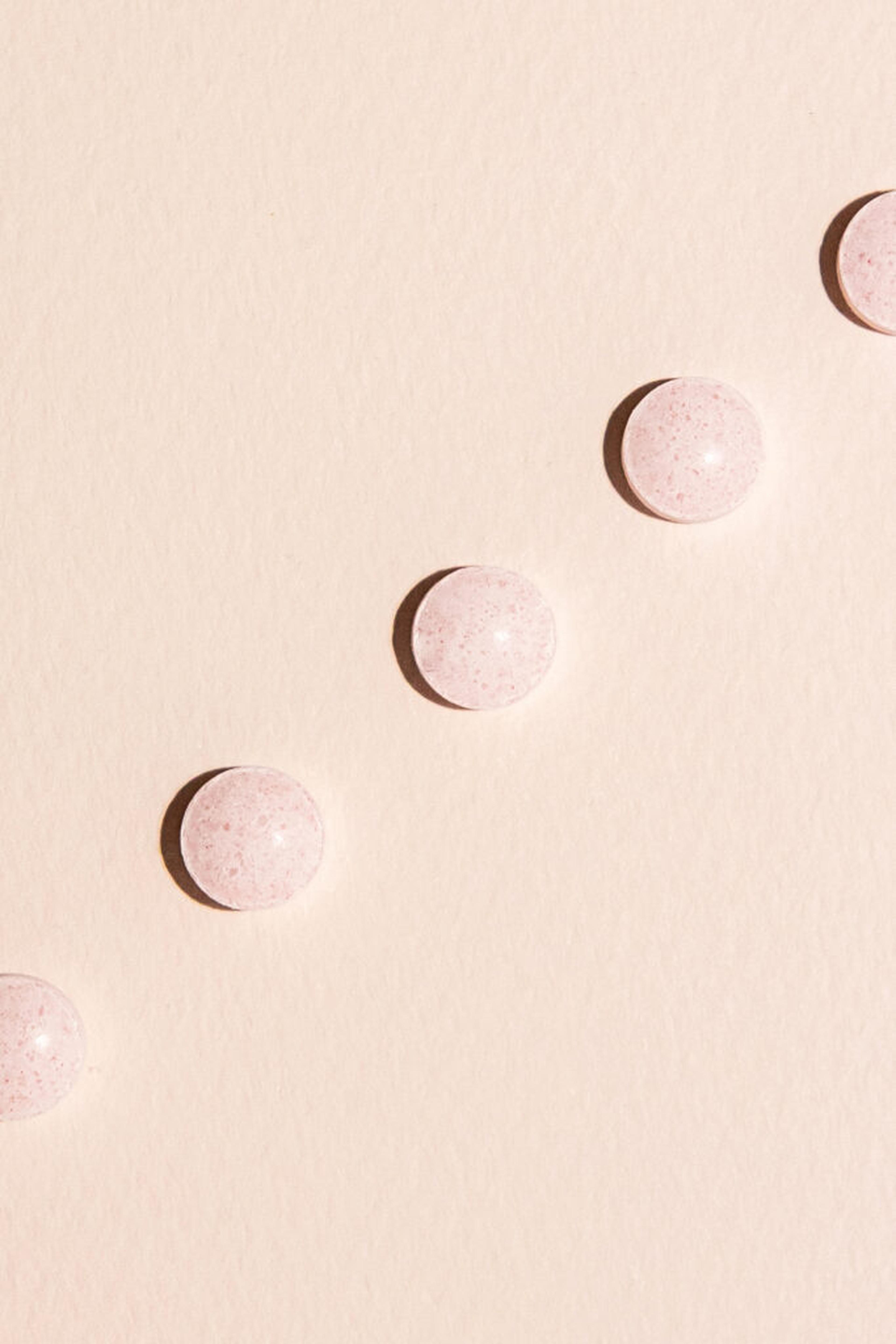 Runda, spräckliga rosa vitamintabletter i en diagonal linje på en ljusrosa yta