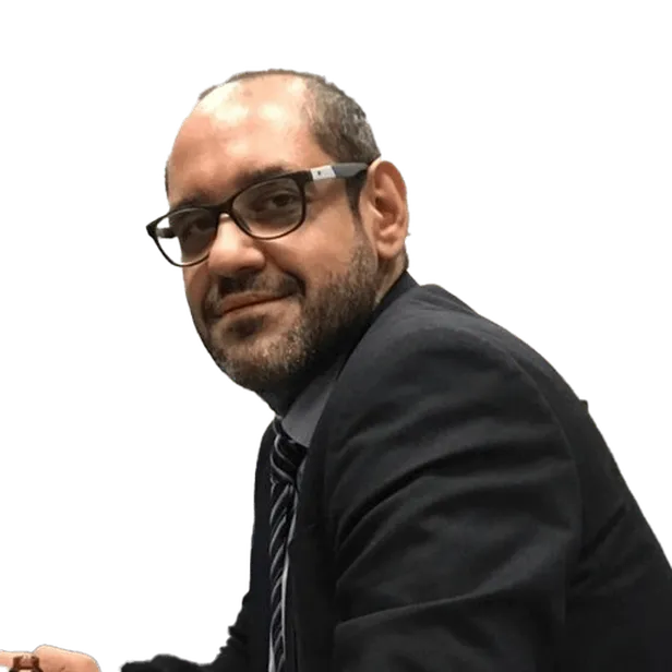 Man with glasses and beard wearing a suit, sitting and smiling.