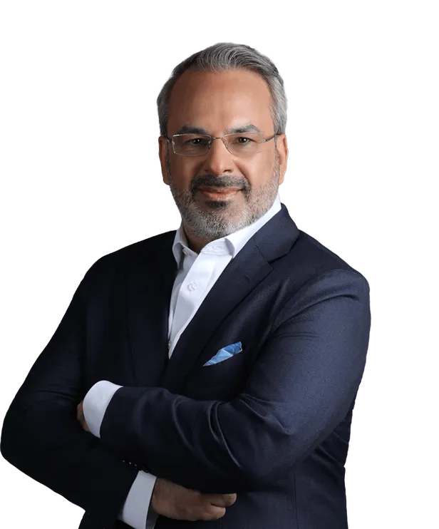 Man with glasses, gray hair, and beard wearing a navy suit and white shirt, arms crossed.