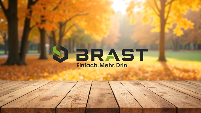Wooden table with "BRAST Einfach.Mehr.Drin." logo, against a blurred background of sunlit autumn trees and fallen leaves.