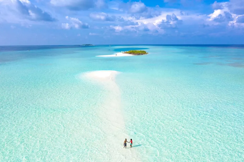 Pareja disfrutando de su luna de miel y caminando por una playa de arena blanca en las aguas cristalinas de las islas Maldivas.