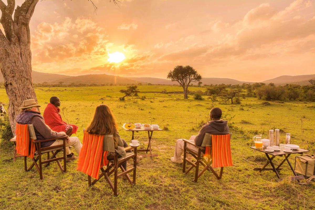 Personas disfrutando de un desayuno al aire libre durante su luna de miel en un safari al amanecer en la sabana africana.