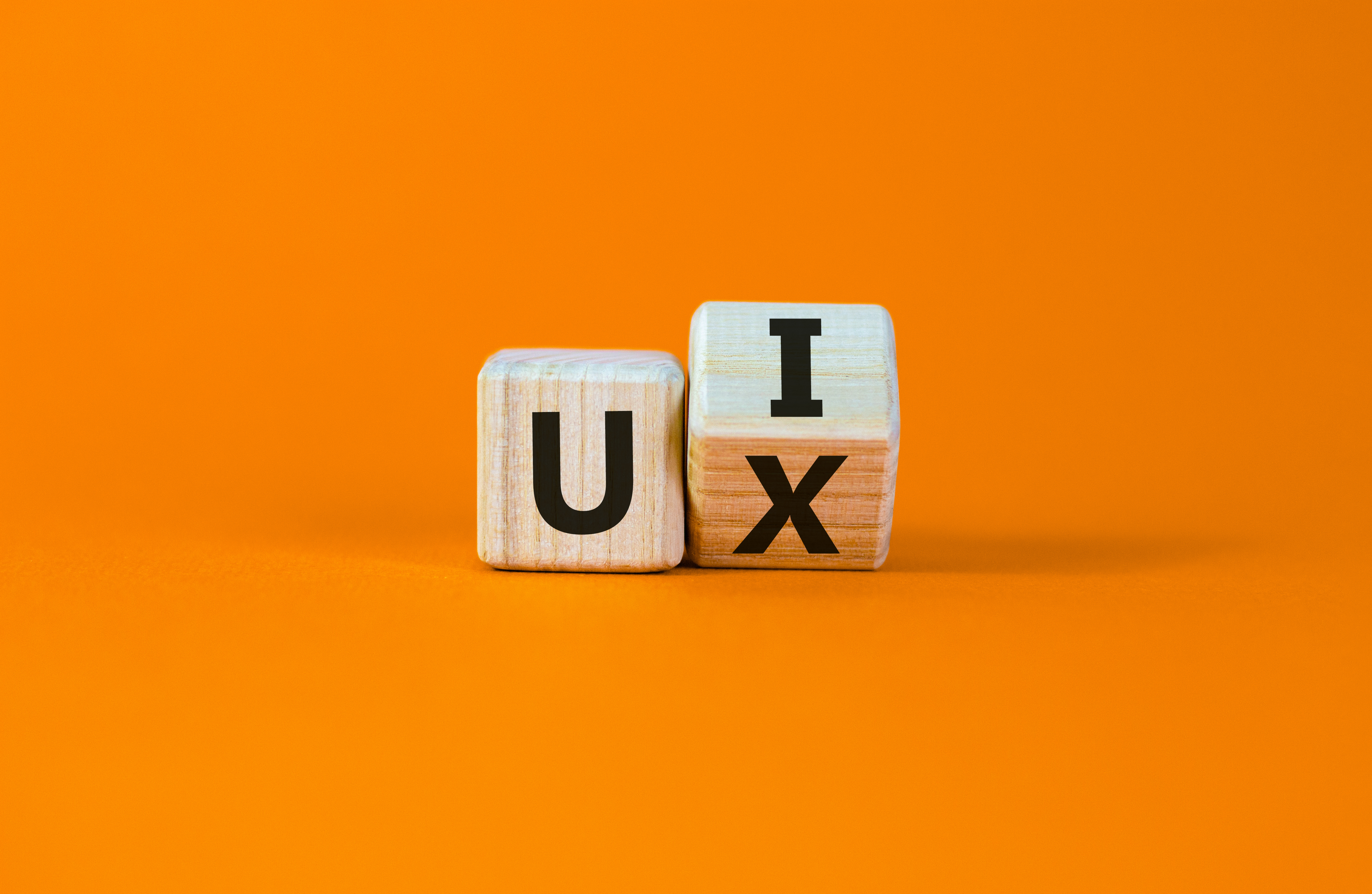 Wooden blocks spelling UX flipping to spell UI on an orange background