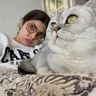 A woman wearing glasses and a cat relaxing on a sofa