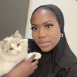 Woman holding a ragdoll cat, looking at the camera in a softly lit room.