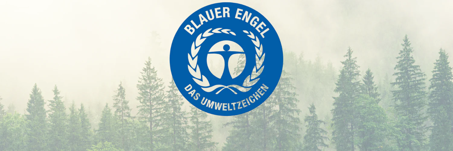 Das Umweltzeichen „Blauer Engel“ vor einem Hintergrund aus nebligem Wald, was für Umweltzertifizierung und Nachhaltigkeit steht.